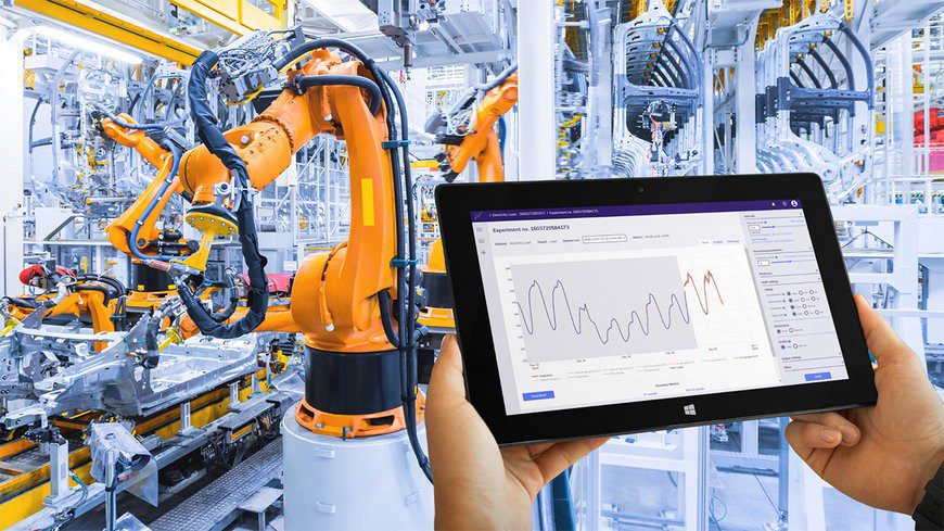 Tablet monitoring data in front of robotic arms in a factory.